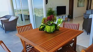 Ein modernes Wohnzimmer mit einem Holzesstisch, vier Stühlen, einem Fernseher und einem Balkon mit Blick.