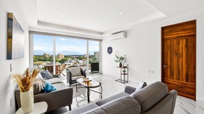 A modern living room with a sofa, chairs, a coffee table, and a view of a cityscape through large windows. - 2-Bedroom Flamingos • Heated Pool • Rooftop (Flamingos)