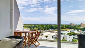 A balcony with a table and chairs, overlooking a cityscape with buildings and greenery. - 2-Bedroom Flamingos • Heated Pool • Rooftop (Flamingos)