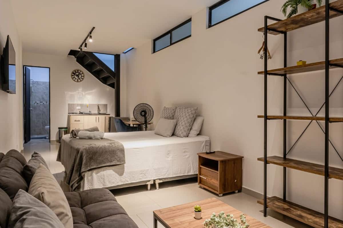 A modern bedroom with a bed, a small desk, a fan, and a staircase.