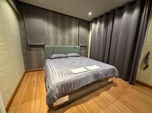 Une chambre d’hôtel moderne avec un grand lit, une literie grise et une tête de lit.