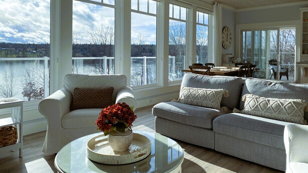 A spacious living room with large windows, a cozy seating area, and a view of a lake. - Lakefront Home on Washademoak Lake with Dock and 255 ft of Water Frontage.     (Coles Island)