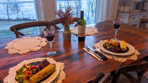 A dining table with a bottle of wine, two glasses of red wine, and plates of food including grilled vegetables and a steak. - Lakefront Home on Washademoak Lake with Dock and 255 ft of Water Frontage.     (Coles Island)