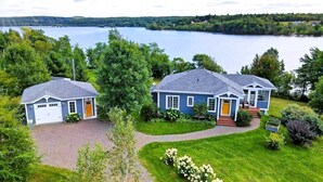 A two-story house with a garage, a covered porch, and a view of a lake. - Lakefront Home on Washademoak Lake with Dock and 255 ft of Water Frontage.     (Coles Island)