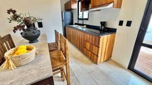 A modern kitchen with wooden cabinets, a built-in stove, and a dining area with a table and chairs. - 2BR Condo Near Beach: Private Jacuzzi & 2 Bikes (Tulum)