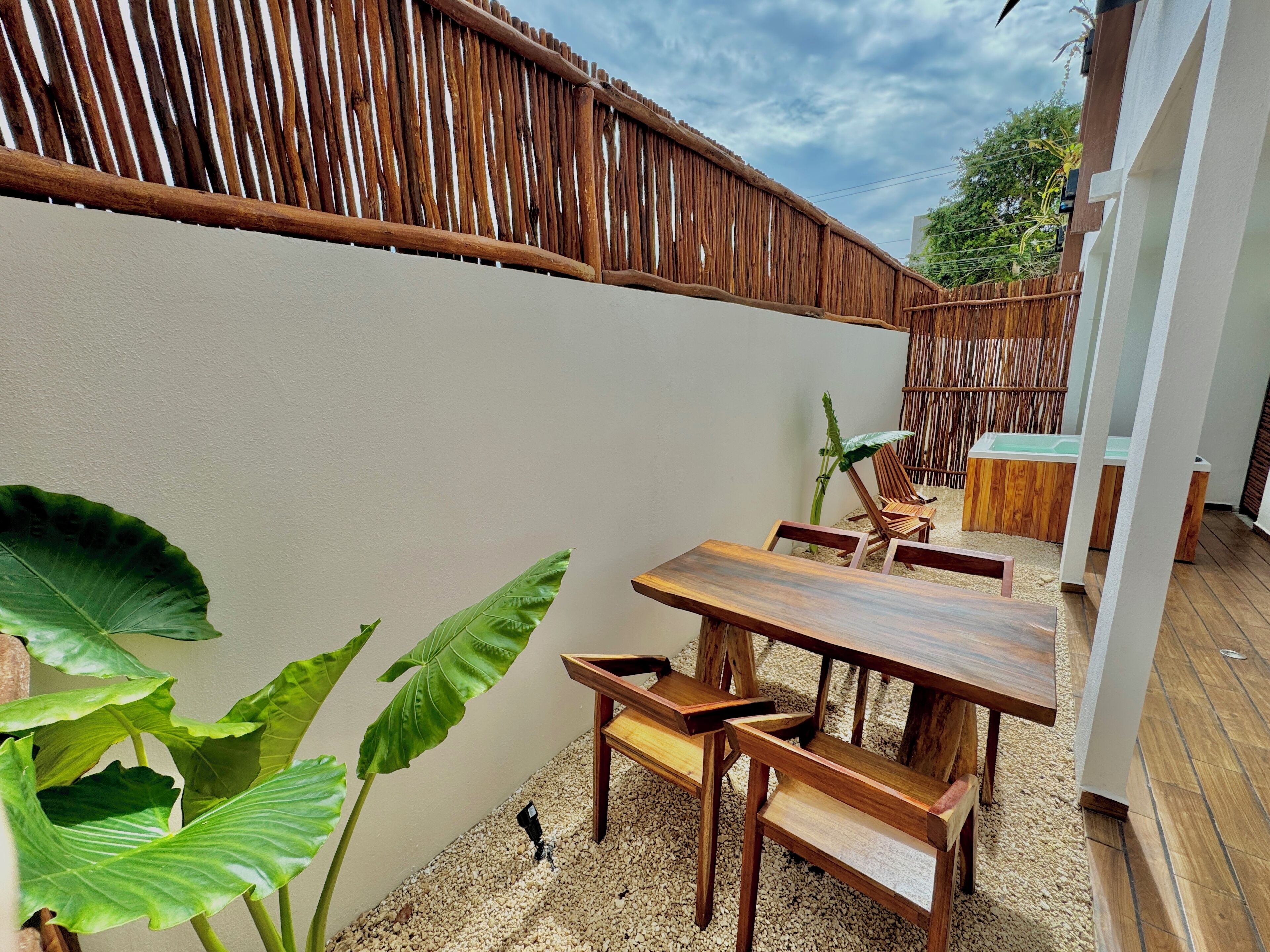 Un patio in legno con tavolo e sedie, una staccionata di bambù e una pianta grande.