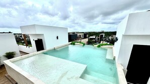 A rooftop infinity pool with a view of surrounding buildings. - 2BR Condo Near Beach: Private Jacuzzi & 2 Bikes (Tulum)