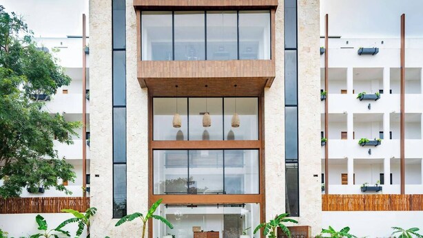 A modern building with a wooden facade, large windows, and balconies with plants. - 2BR Condo Near Beach: Private Jacuzzi & 2 Bikes (Tulum)