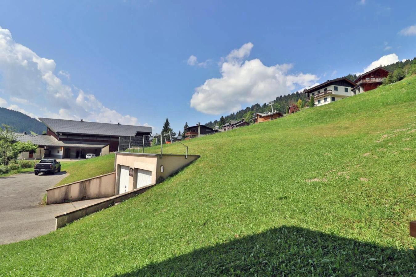 Une propriété située sur une colline, comprenant un bâtiment moderne, un espace de stationnement et une pente herbeuse.