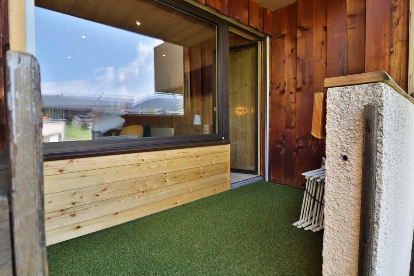 A room with a large window, wooden walls, and a green artificial turf floor.