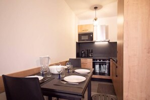 A compact kitchen with a microwave, coffee maker, and oven. A dining table with chairs is set for two.