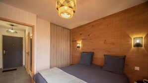 Een slaapkamer met een groot bed, twee bedlampen, een houten hoofdbord en een deur naar een andere kamer.