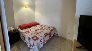 A small, neatly arranged bedroom with a bed, a nightstand, a lamp, and a TV.