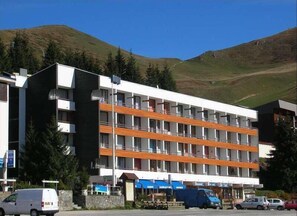 Een hotel met meerdere verdiepingen, balkons, een parkeerplaats en een bergachtige achtergrond.