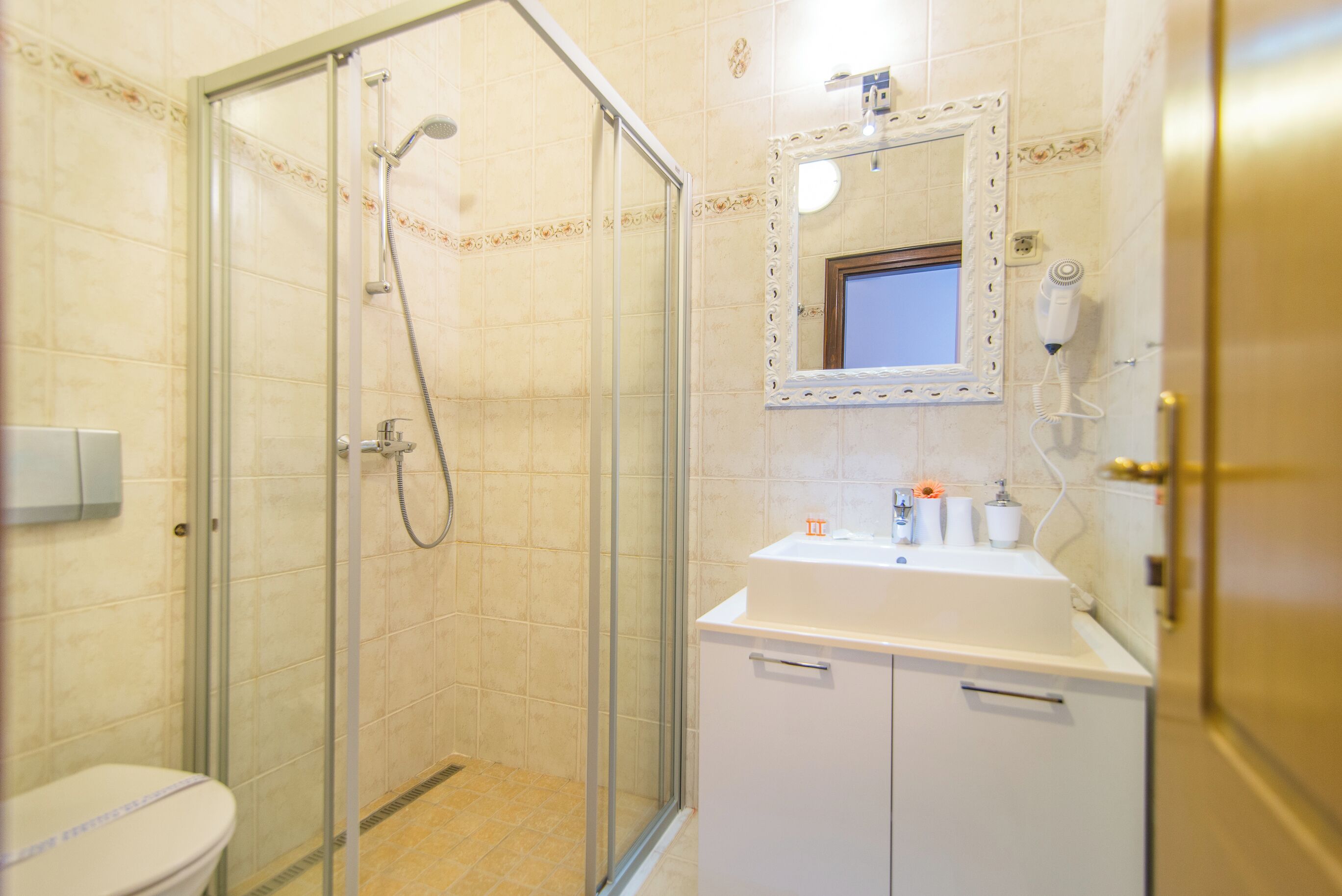 Ein Badezimmer mit einer Duschkabine, einer Toilette, einem Waschbecken mit Spiegel und einem an der Wand befestigten Föhn.