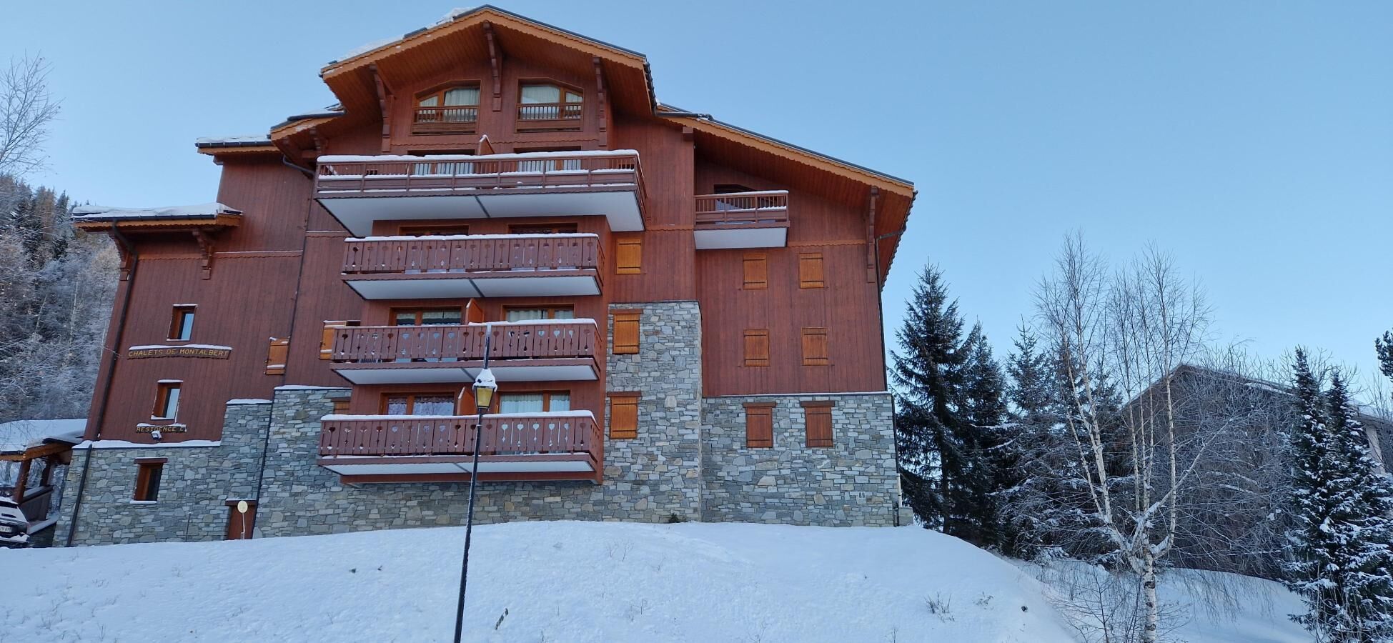Un hôtel à plusieurs étages, doté de balcons et d’une façade en pierre, entouré d’arbres couverts de neige.