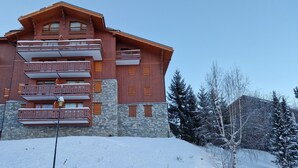 Ett hotell med flera våningar, balkonger och en fasad av sten, omgivet av snötäckta träd.