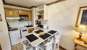 A compact kitchen with white cabinetry, a microwave, a toaster, and a dining table with four chairs. - 100m from ski slopes, 1st floor, view ski slopes, balcony, tv, 35m², Montalbert (La Plagne)