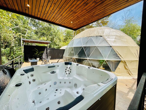 A hot tub with multiple jets, a covered seating area, and a dome tent in a garden setting. - Escápate al paraíso Domos con jacuzzi y terraza privada dentro de la naturaleza (Cóbano)