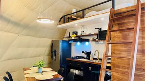 Une cuisine compacte équipée d’un réfrigérateur intégré, d’une cuisinière et d’un évier. On y trouve une table à manger avec des chaises et une petite plante en pot.