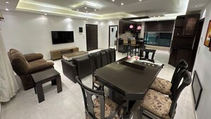 Ein modernes Wohnzimmer mit Essbereich, einem wandmontierten Flachbildfernseher und einer Küche im Hintergrund.