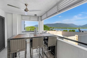 Un balcone con tavolo e sedie, una ventola a soffitto e vista su un lago e montagne.