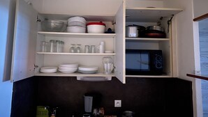 Una cocina con armarios abiertos que muestran vajilla, vasos y utensilios de cocina.