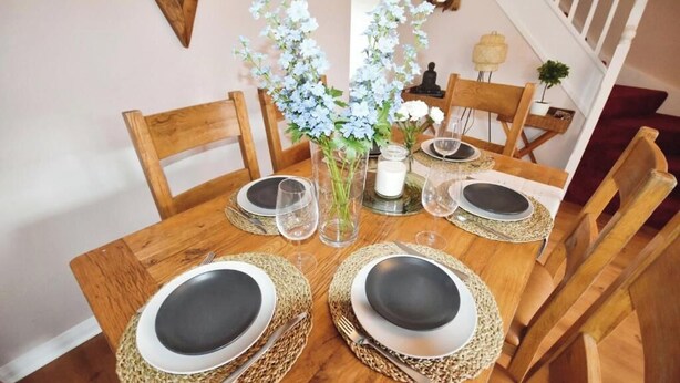 Une table de salle à manger en bois, mise avec des assiettes, des couverts et un vase de fleurs.