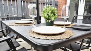 Un espace de restauration en plein air avec une table dressée pour deux personnes, agrémentée de sets de table en fibres tressées, d’assiettes et de verres.