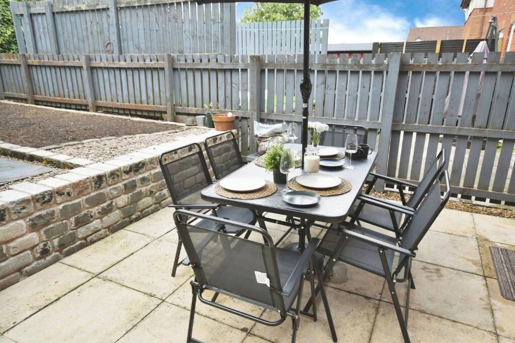 A patio with a table set for four, surrounded by chairs, and a wooden fence in the background.