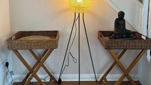 Un escalier avec une lampe fixée au mur, deux petites tables d’appoint en osier et une statue.