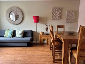 A living room with a sofa, a dining table with chairs, a red floor lamp, and wall art.
