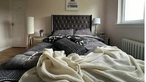 Une chambre à coucher avec une tête de lit capitonnée, un grand lit avec une literie à motifs, une table de chevet avec une lampe et une fenêtre donnant sur un beau paysage.