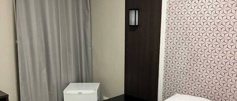 A hotel room with a bed, a nightstand, a small white appliance, and a towel rack.
