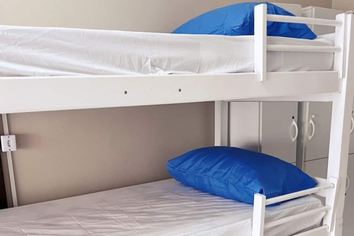A bunk bed with a white frame, a lower bed with a blue pillow, and a wardrobe with two doors.