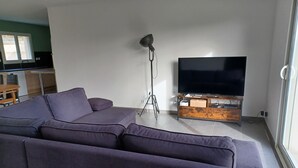 A modern living room with a sectional sofa, a flat-screen TV on a wooden stand, and a floor lamp. - Charming new house with terrace and garden (Muron)