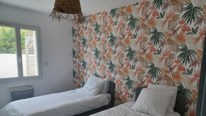 A bedroom with two single beds, a window, and a wall with a tropical leaf pattern. - Charming new house with terrace and garden (Muron)