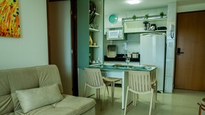 A compact living space with a kitchenette, a dining area with a glass table, and a beige sofa. - Magnific (João Pessoa)