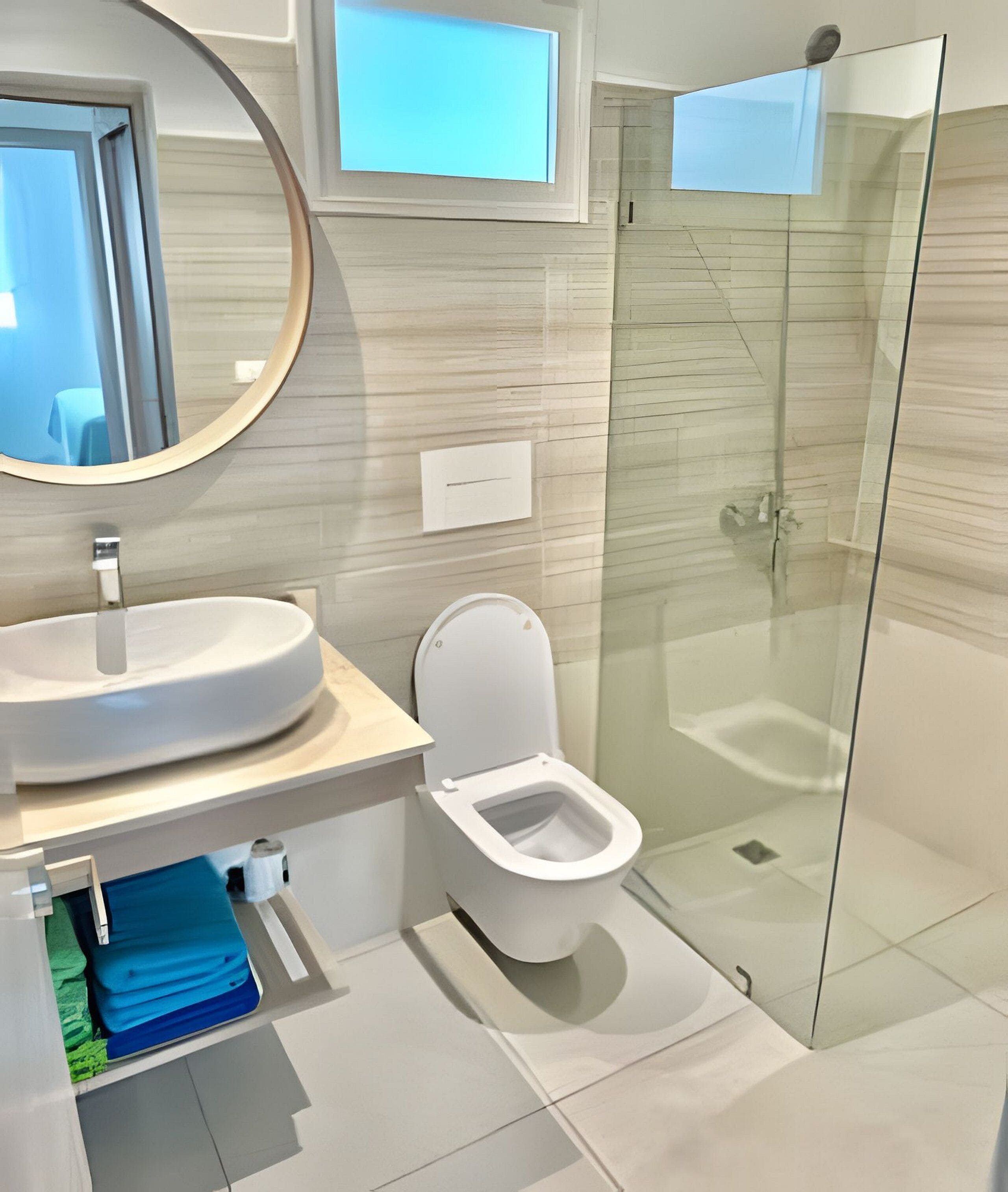 A modern bathroom with a round mirror, a sink, a toilet, and a glass-enclosed shower.