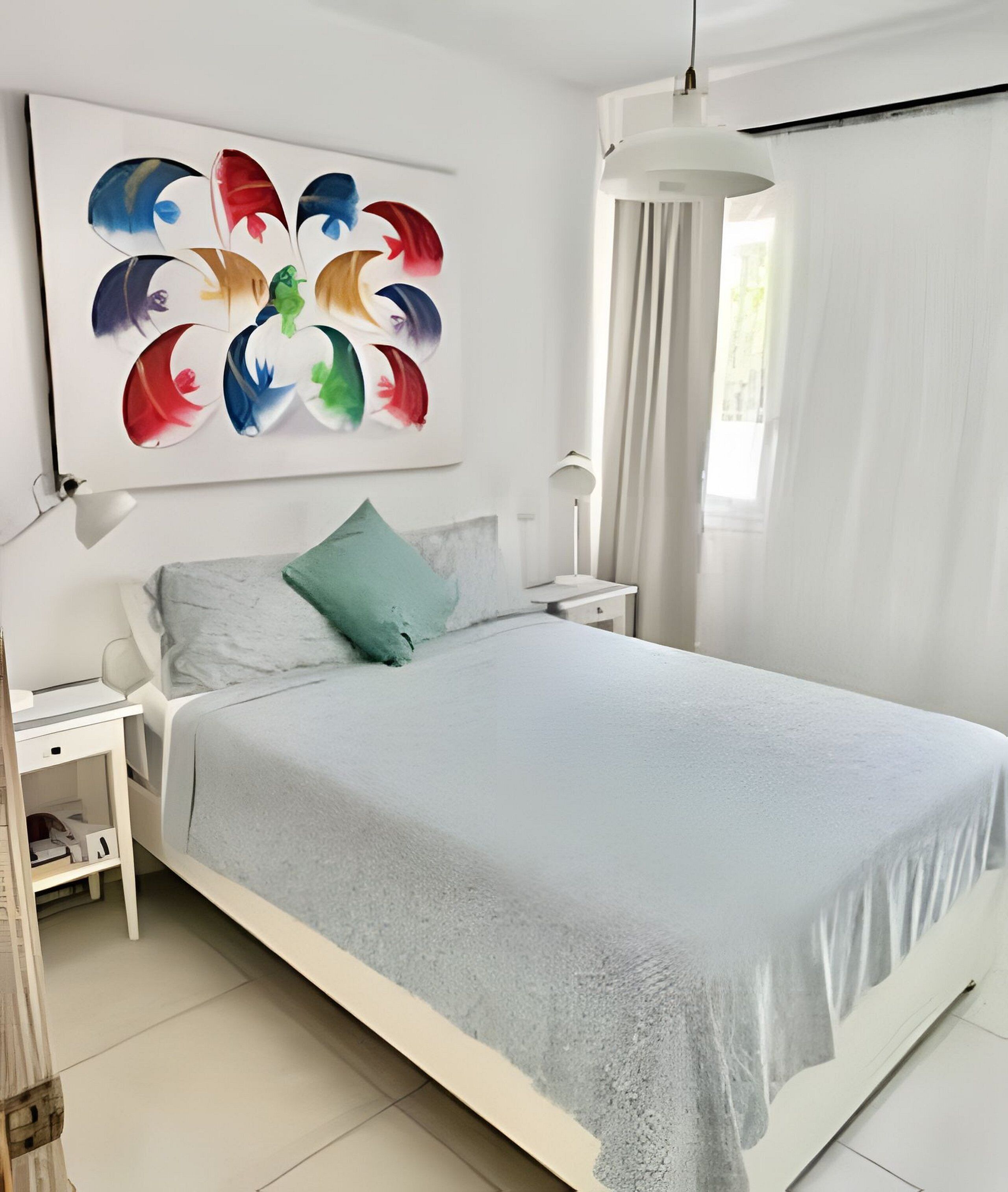 A modern bedroom with a bed, a nightstand, a lamp, and a wall art piece.