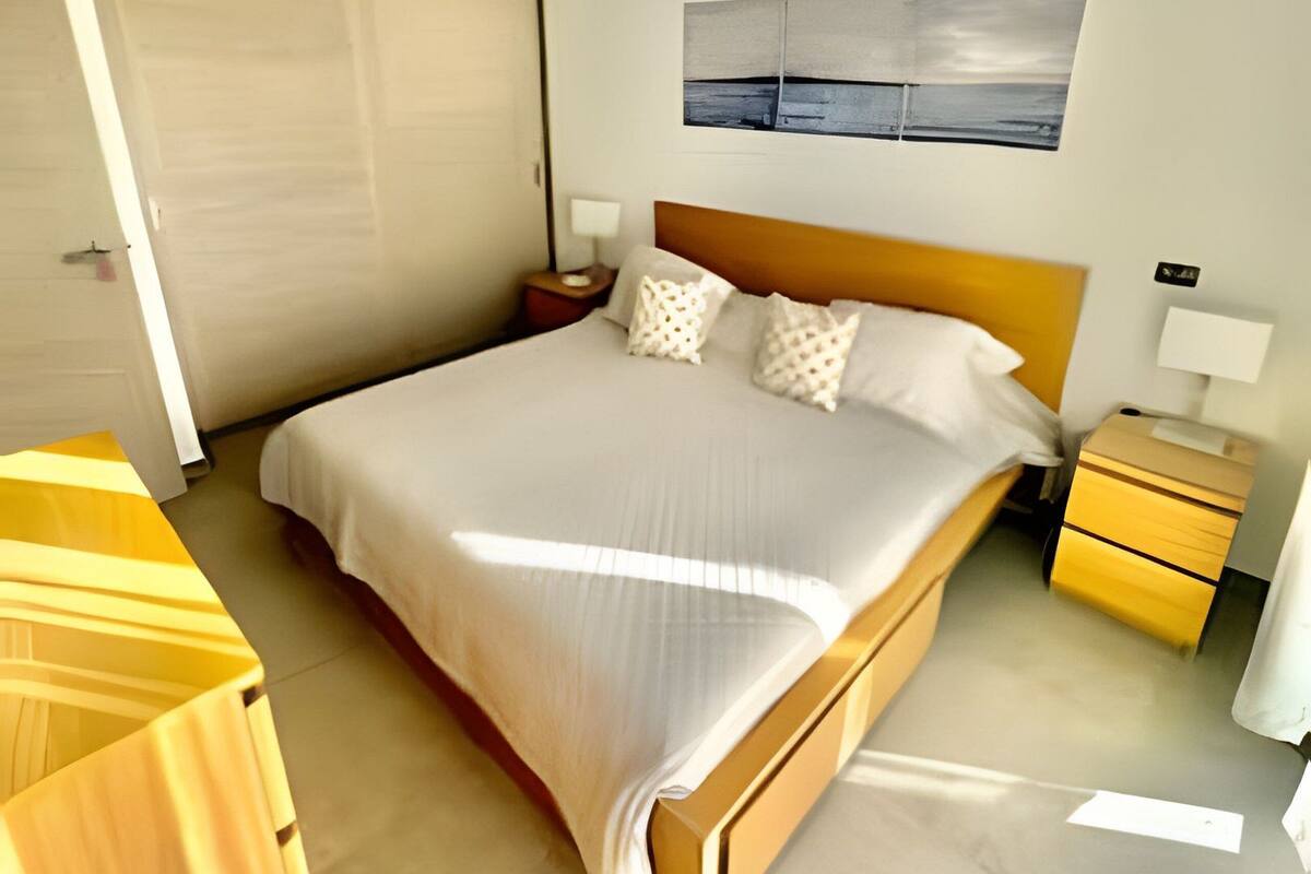 A modern bedroom with a large bed, wooden headboard, and a nightstand with a lamp.