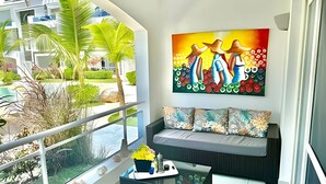 A balcony with a sofa, a glass coffee table, and a painting.