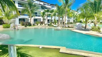 A resort pool with clear blue water, surrounded by palm trees and lounge chairs.