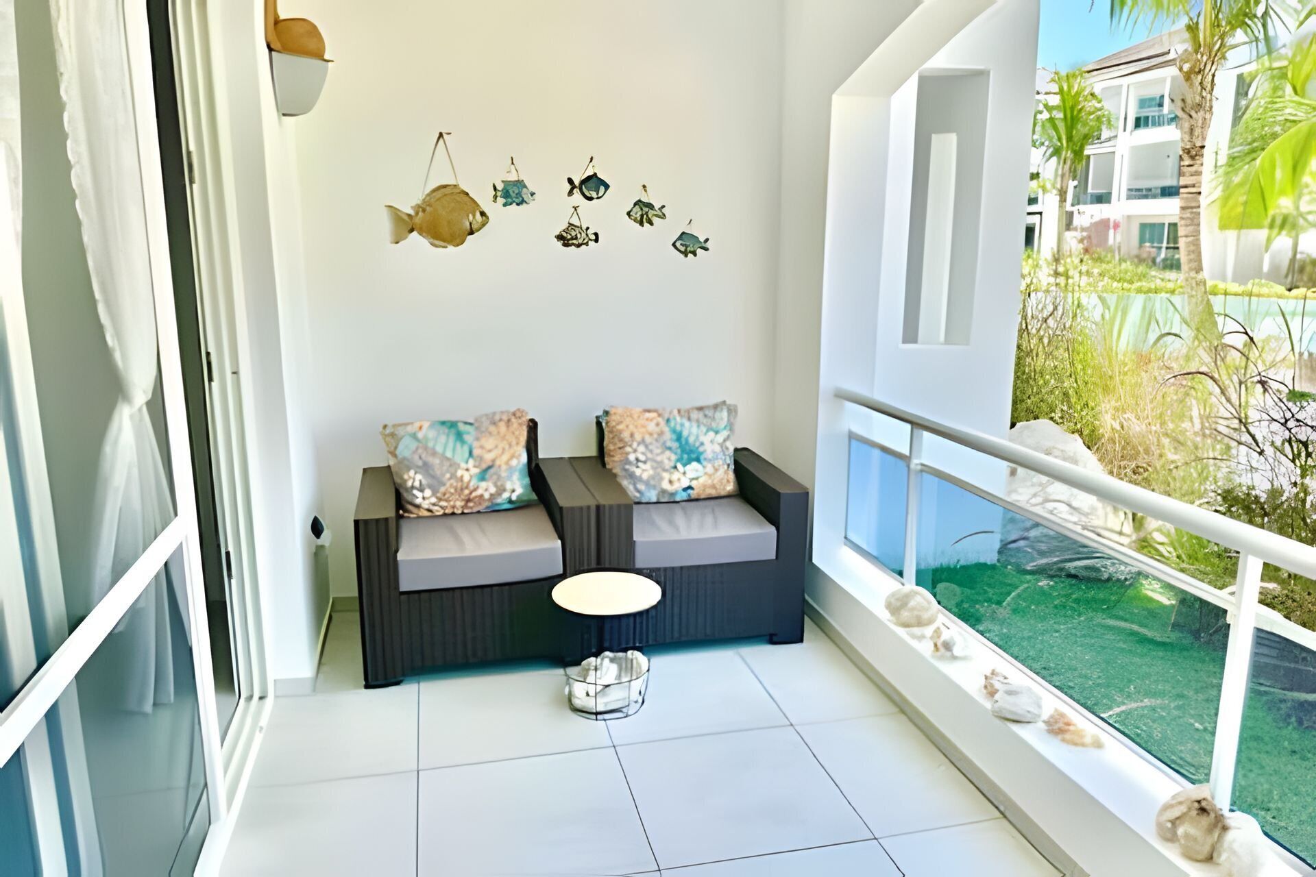 Un balcon avec un canapé, des coussins, une petite table et une vue sur un immeuble et des espaces verts.