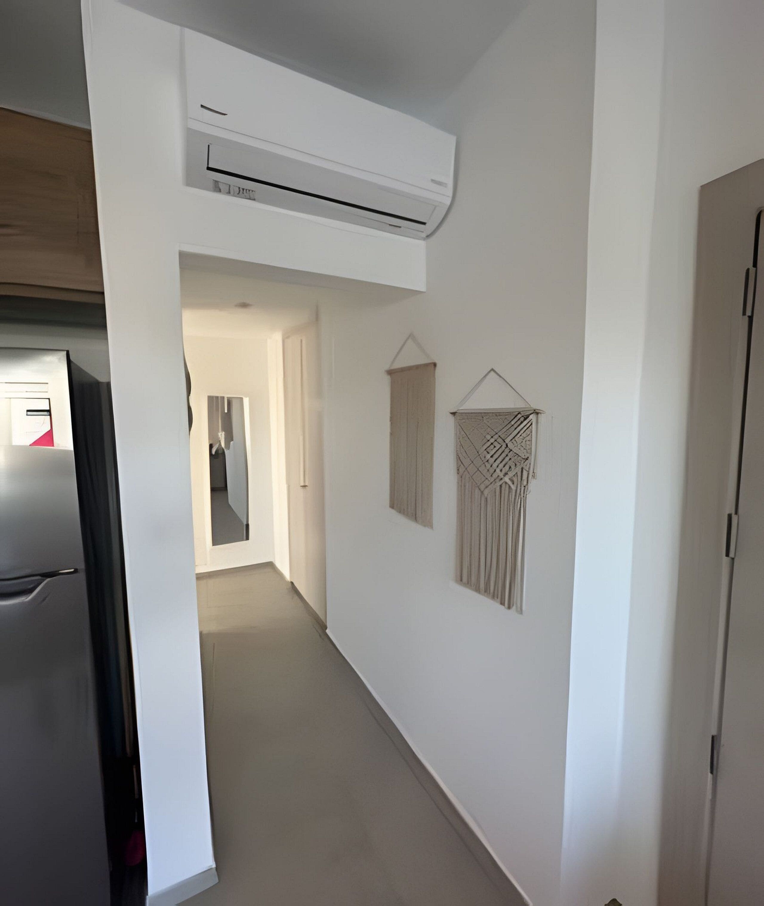 A hallway with a white air conditioning unit, a door, and two macramé wall hangings.