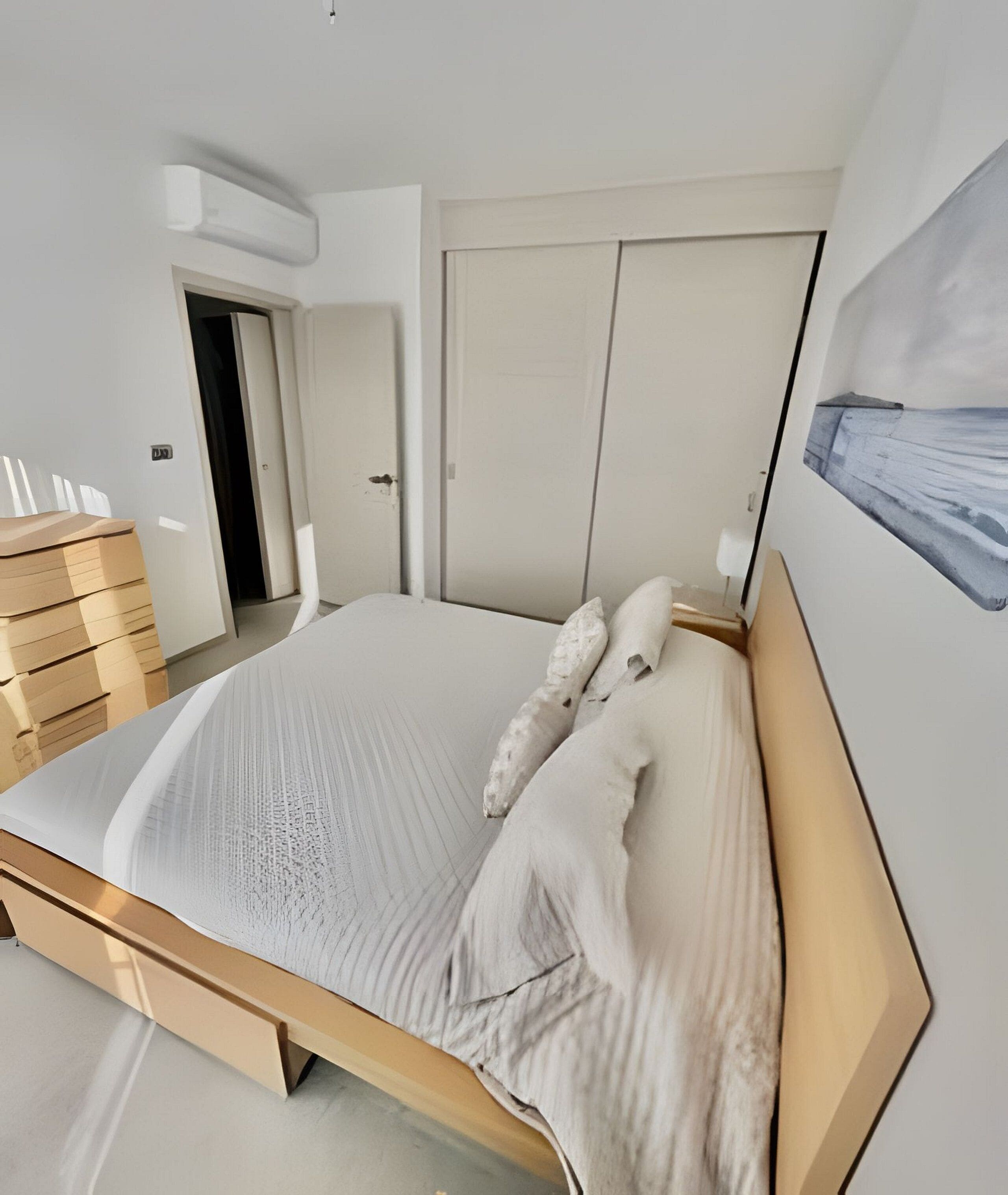 A modern bedroom with a large bed, wooden headboard, and a painting on the wall.