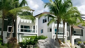 A modern multi-story building with a flat roof, surrounded by lush green grass and palm trees.