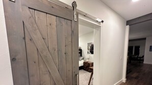 Una habitación con una puerta corrediza de madera estilo granero, una pared blanca, un escritorio pequeño con una silla y suelo alfombrado.