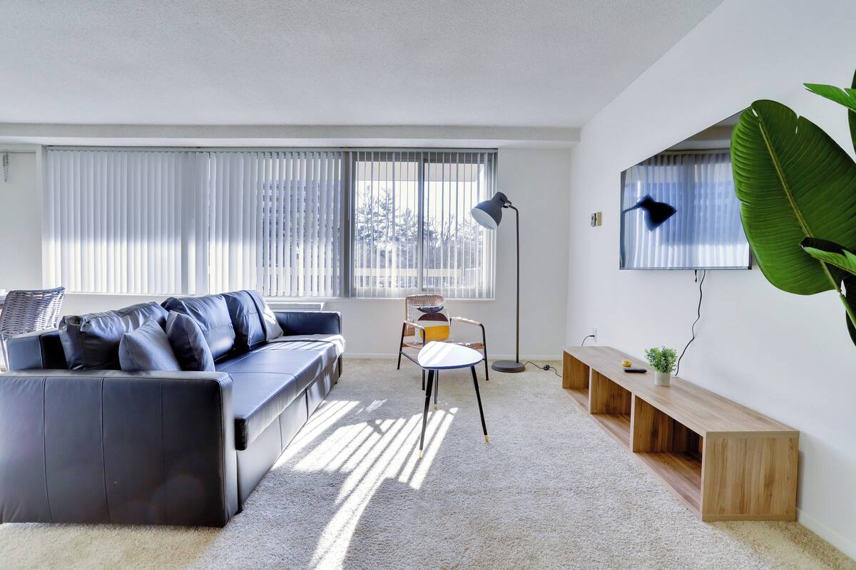 A modern living room with a black leather sofa, a wooden bench, a small table, and a floor lamp.