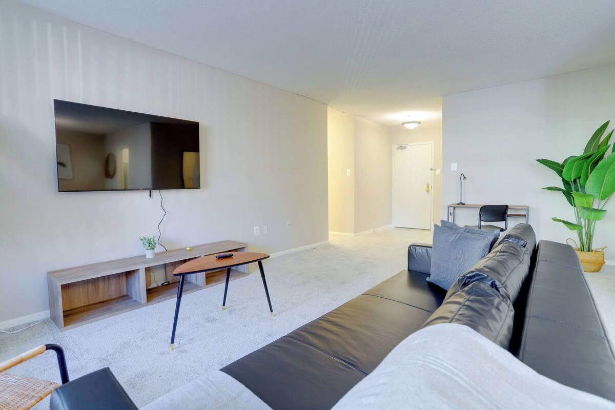 A modern living room with a large flat-screen TV, a sofa, a coffee table, and a potted plant.